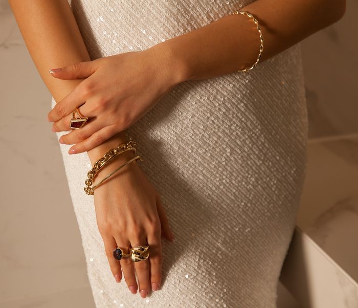 Nahaufnahme der geschmückten Hände einer Person auf einem Paillettenkleid, auf dem eleganter Schmuck zu sehen ist.