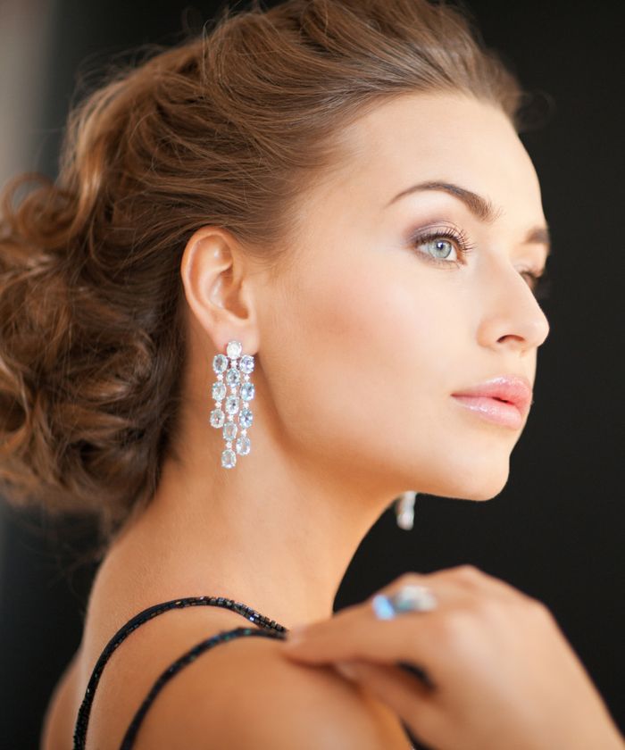 Frau mit funkelnden Ohrringen und dunklem Kleid, seitlich betrachtet.